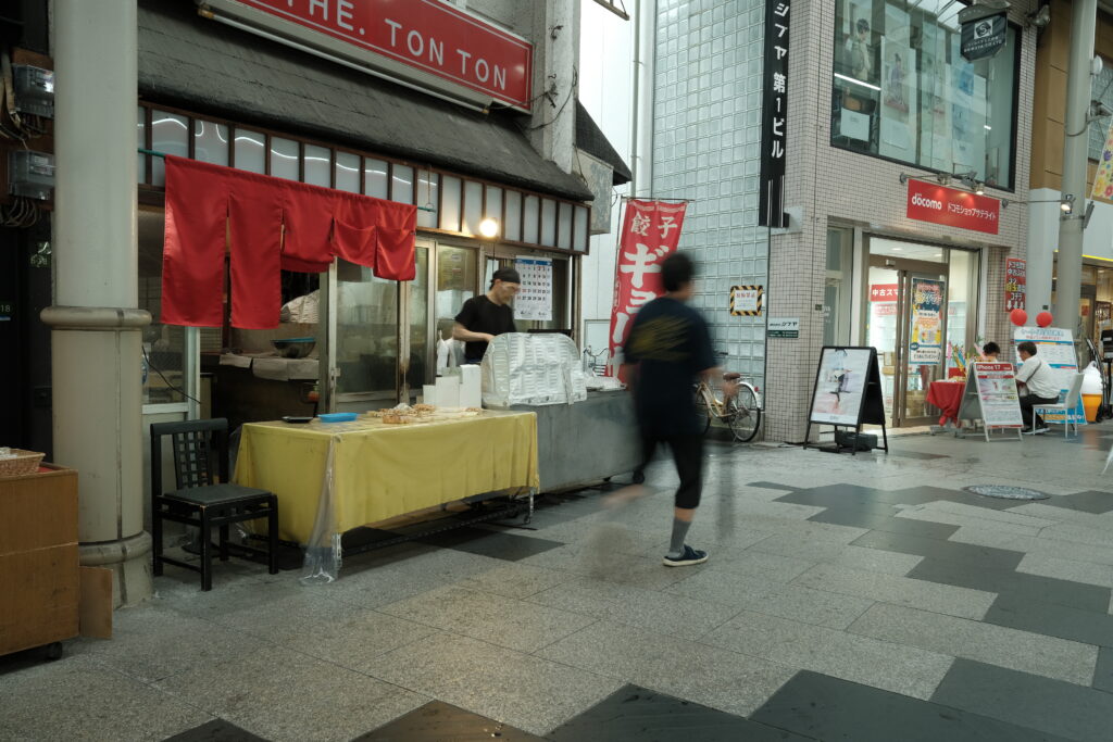 商店街のアーケードでシャッタースピード1/8秒のスローシャッターにより人の動きを残像で捉えた写真