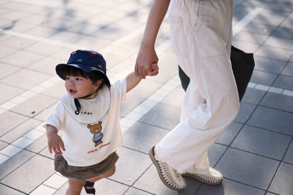 母親と手を繋いで歩く子供。富士フイルムのカメラで撮影。